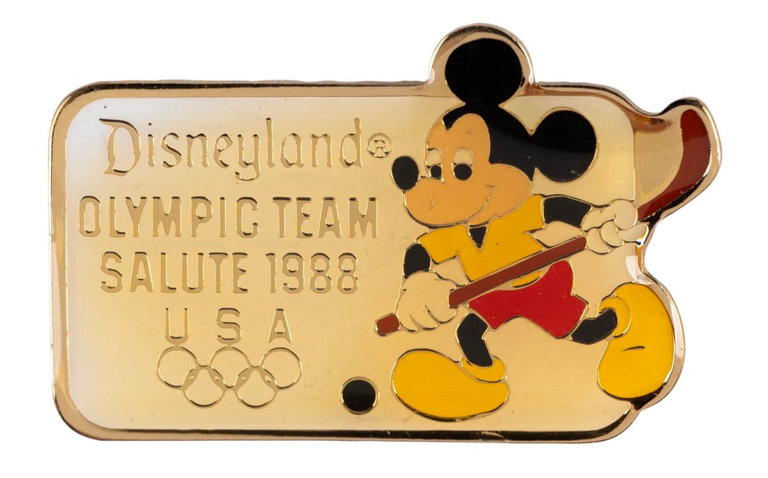 A Mickey Olympic Field Hockey Pin.: (Disneyland, 1988) A Disneyland Olympic Team Salute 1988 pin, featuring Mickey Mouse playing field hockey. Measuring 1.5" wide, the pin is in very good condition with color shift from age.