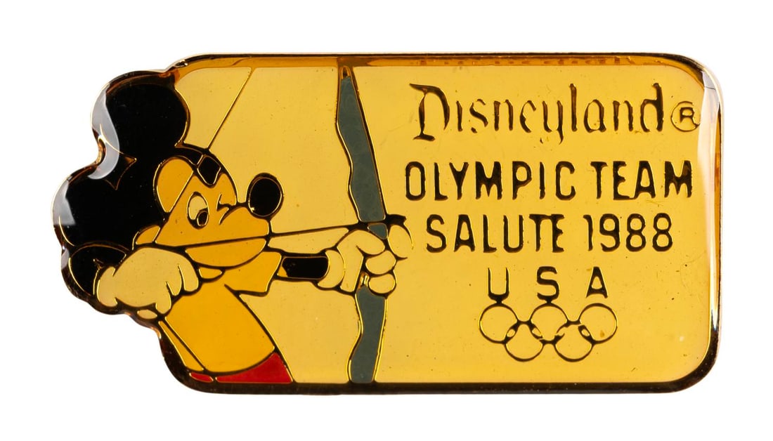 A Mickey Olympic Archery Pin.: (Disneyland, 1988) A Disneyland Olympic Team Salute 1988 pin, featuring Mickey Mouse as an archer. Measuring 1.5" wide, the pin is in very good condition with color shift from age.