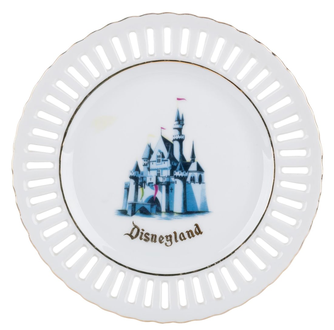 A Sleeping Beauty Castle Souvenir Lace Plate.: (Disneyland, 1960s-70s) A souvenir decorative plate featuring Sleeping Beauty Castle and a slotted pattern with a gold accent. Measuring 7.25" in diameter, the plate is in good condition with sticker