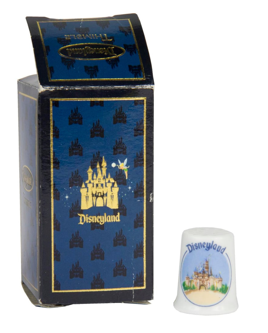 A Disneyland Sleeping Beauty Castle Thimble.: (Disneyland, 2000s) A Disneyland thimble featuring Sleeping Beauty Castle, in its original blue Disneyland Castle box. Measuring 0.75" in diameter and 1" tall, the thimble is in fine condition with a