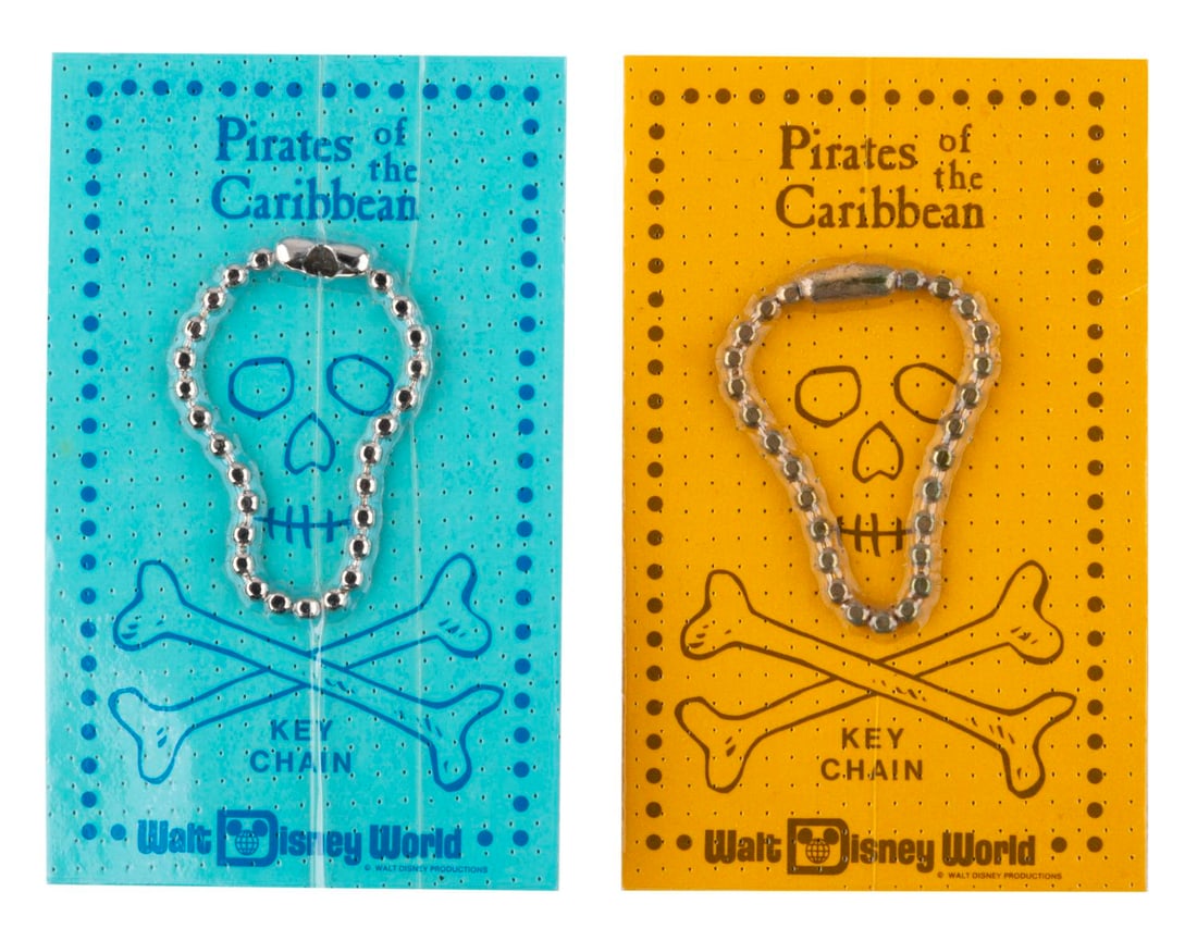 A Pair of Pirates of the Caribbean Key Chains.: (Walt Disney World, 1973) A pair of Pirates of the Caribbean Key Chains from Walt Disney World. The pair of ball keychains on gold and blue carding are among the earliest of the related attraction sou