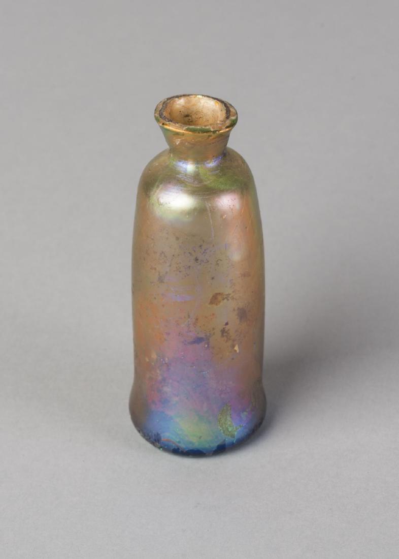 A cylindrical unguentarium glass bottle, possibly late: A cylindrical unguentarium glass bottle, possibly late Roman, of balustre form, with purple and green iridescence, 9cm. high