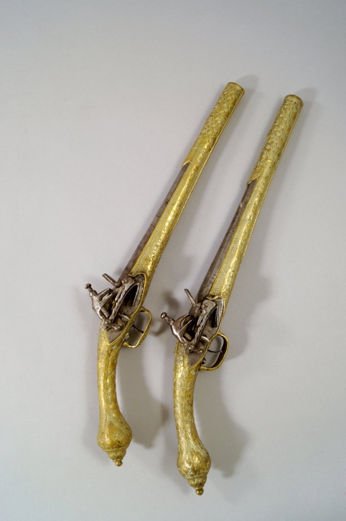A pair of Turkish flintlock pistols with steel barrels: A pair of Turkish flintlock pistols with steel barrels and locks, with decorative brass full stocks and rat tail handles with ovoid pommels, 51 cm long