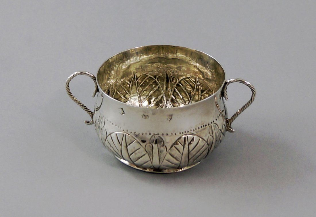 A late Commonwealth silver porringer, London c.1657,: A late Commonwealth silver porringer, London c.1657, maker's mark rubbed, of bulbous form with leaf embossed decoration, embossed Tudor rose to base and rope twist handles, approx 5.2cm high, approx 2