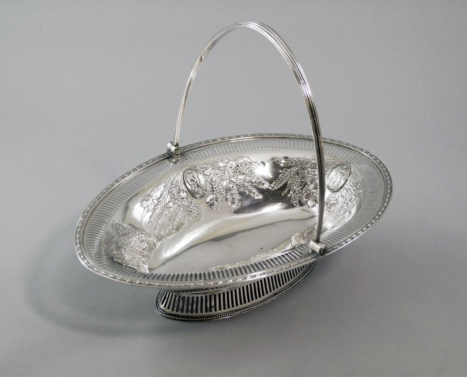 A George III silver swing handled fruit bowl, London: A George III silver swing handled fruit bowl, London c.1782, maker's mark rubbed but possibly Benjamin Laver, of navette form with pierced border, embossed with grape vines and ears of wheat, applied 