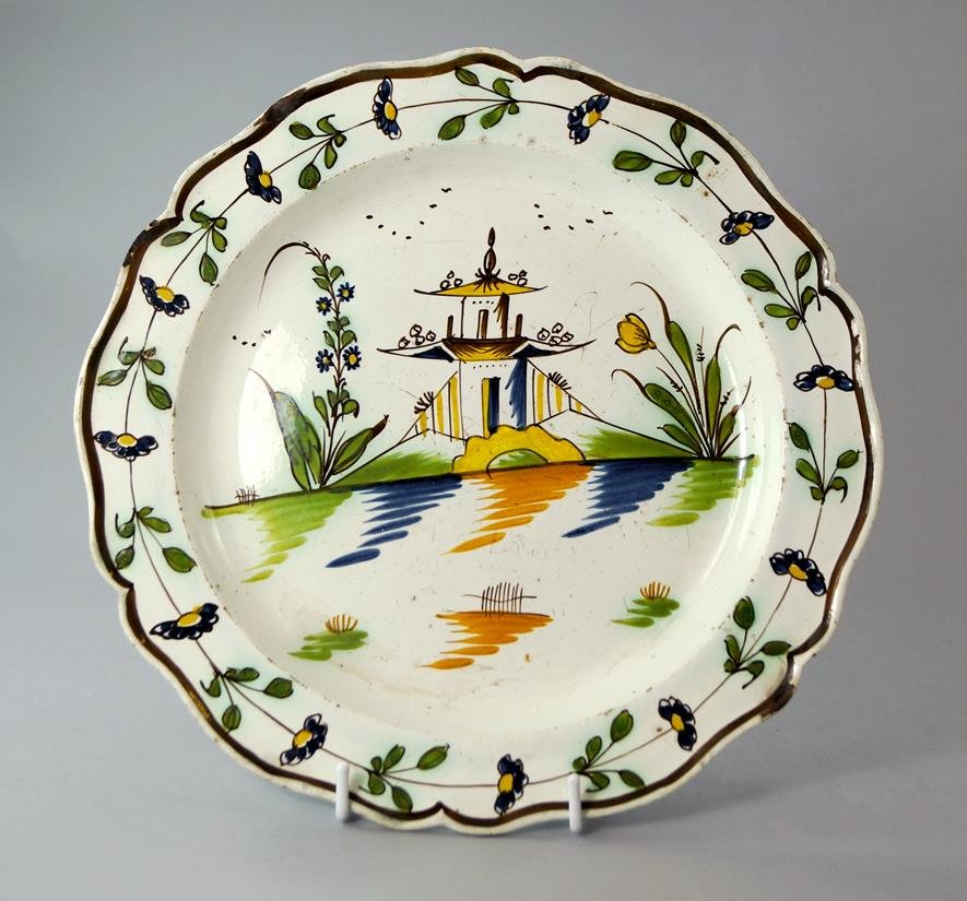 A Continental tin glazed earthenware plate, possibly: A Continental tin glazed earthenware plate, possibly French, late 17th/ early 18th century, centrally painted with pogoda in Chinoiserie landscape, the rim with a continuous design of flowers and foli