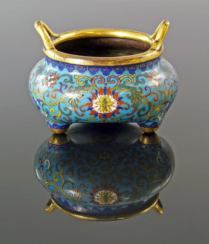 A Chinese enamel twin handled incense burner, Qianlong,: A Chinese enamel twin handled incense burner, Qianlong, resting on three feet, decorated with flowers and trailing foliage, 11cm. diameter