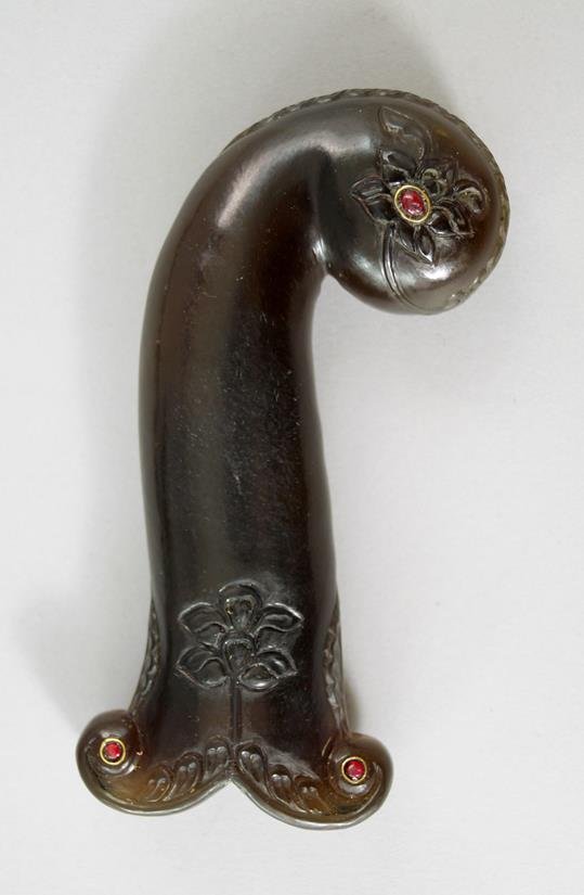 A Mughal jade dagger handle, carved with stylised: A Mughal jade dagger handle, carved with stylised flowers and leaves, mounted with red enamel cabouchons, 13cm. long