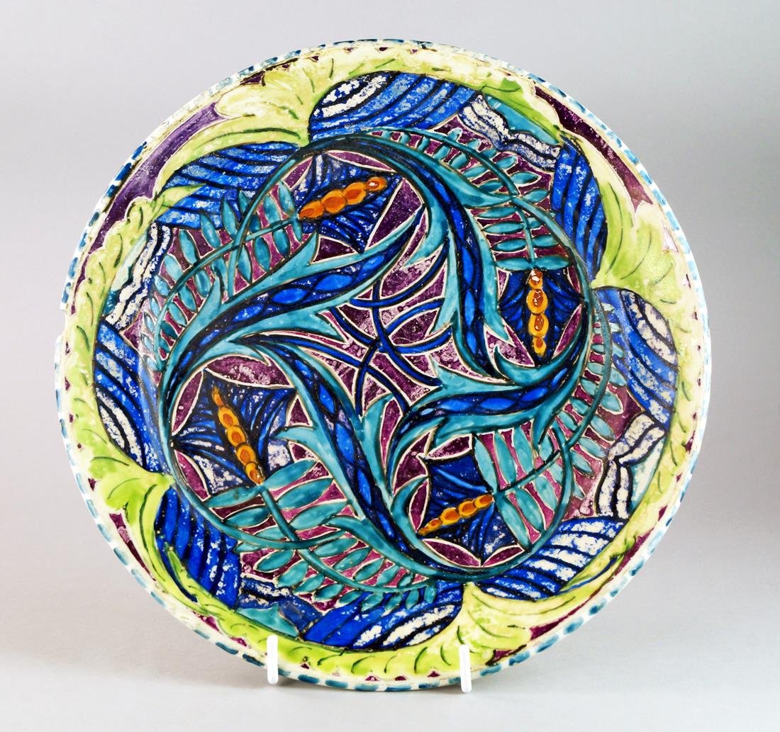 John Pearson, British, 1885-1910, a ceramic cold: John Pearson, British, 1885-1910, a ceramic cold painted dish, applied to the recto with stylised leaves, the verso with a bird design, signed with initials, 32.9cm dia