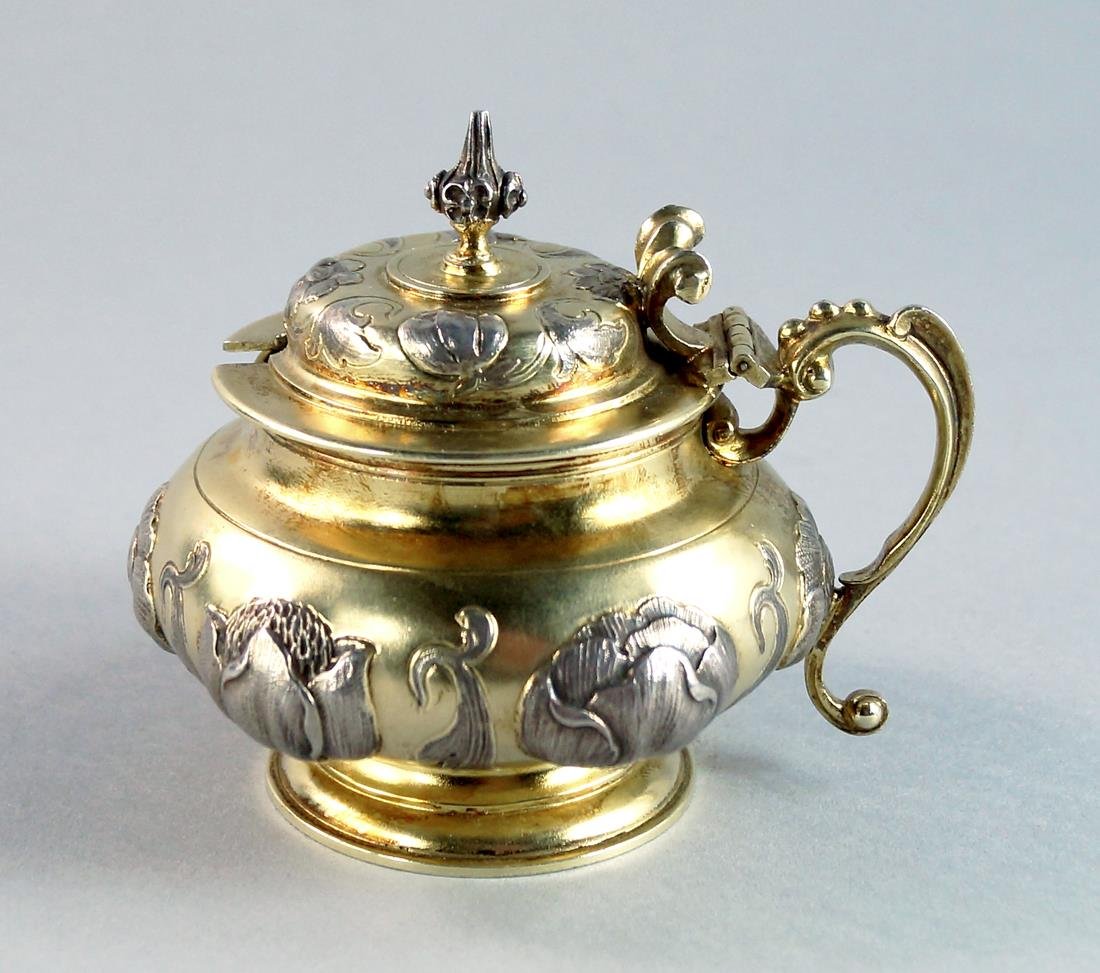 A Victorian parcel-gilt silver mustard pot, London: A Victorian parcel-gilt silver mustard pot, London c.1867, George Fox, of squat circular form with flattened dome cover and floral decorated knop finial, chased in relief with large tulips and other f