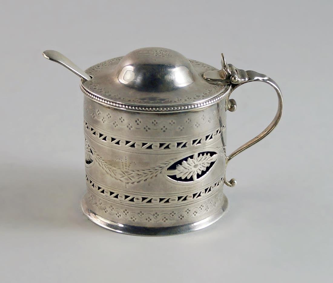 A George III silver drum mustard, London 1784, Thomas: A George III silver drum mustard, London 1784, Thomas Daniell, the domed cover engraved with crest over initial D, beaded rim and bright cut decoration, pierced bands of vitruvian scrolls and pierced
