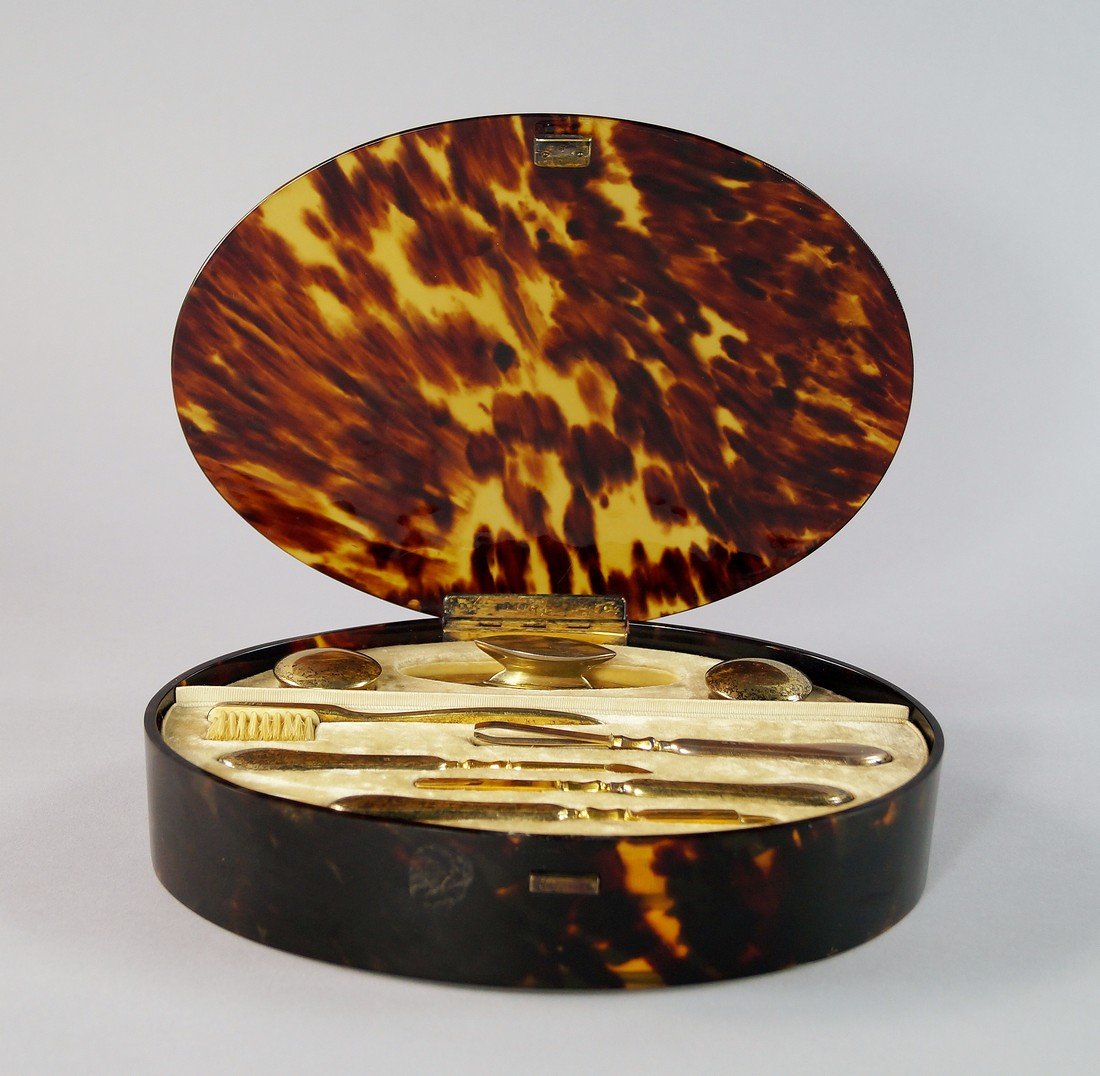An oval tortoise shell and silver gilt travelling: An oval tortoise shell and silver gilt travelling manicure set, early 20th century, to contain nail buffer, two make up pots, tooth brush, clippers, cuticle knife, file and other tools, marks for CD L