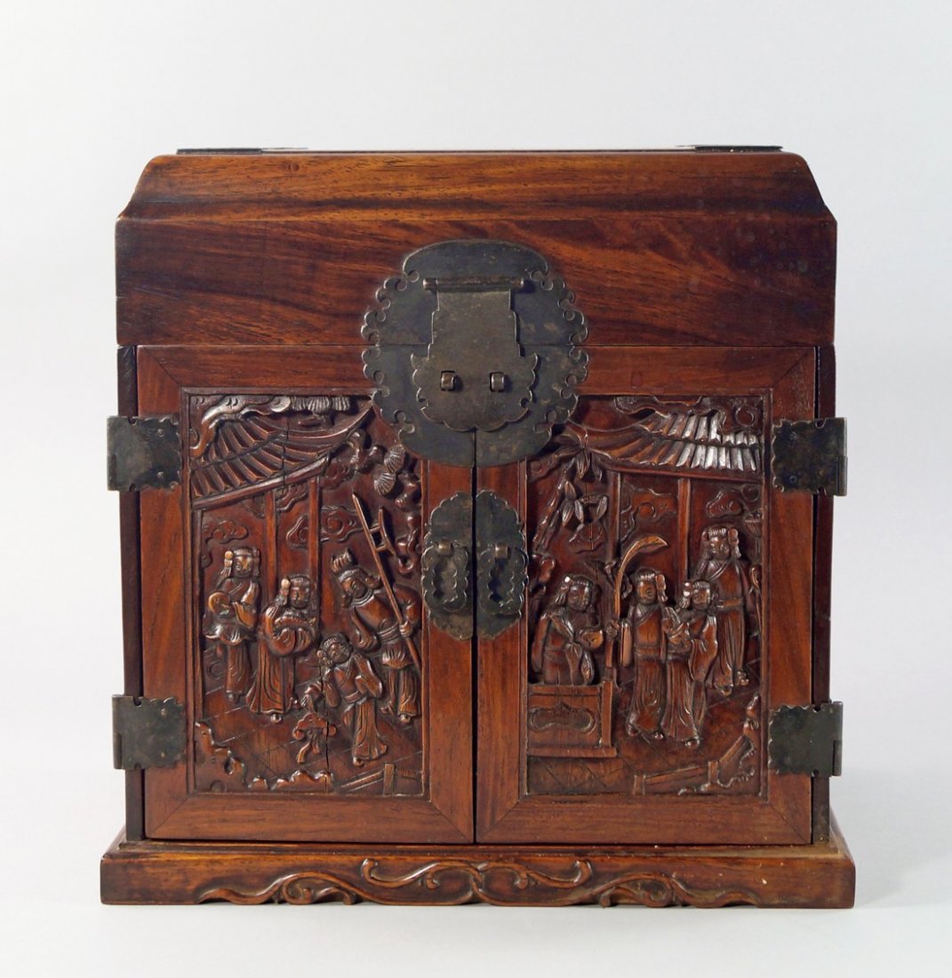 A Chinese hardwood table cabinet, 20th century, with: A Chinese hardwood table cabinet, 20th century, with lifting lid to reveal a tray surface, above two panel doors carved with figures in interiors, enclosing drawers, on a plinth base, 32.5cm high