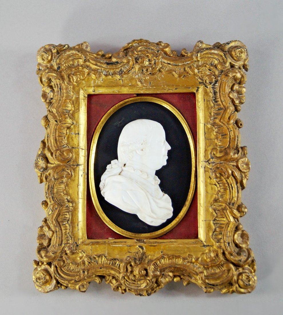 In the style of James Tassie, a moulded white glass: In the style of James Tassie, a moulded white glass paste portrait bust of a man, 19th century, modelled in profile, with hair in a chignon, dressed in robes and armour, moulded to the shoulder with t