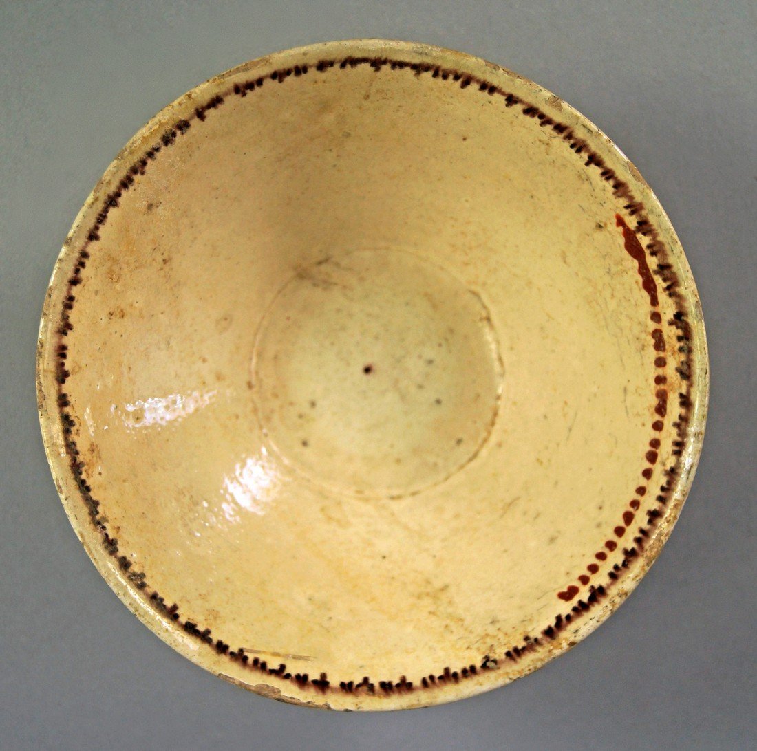 A Persian cream glazed pottery bowl, of conical form,: A Persian cream glazed pottery bowl, of conical form, the edge with continuous double red dot border, 15cm diam