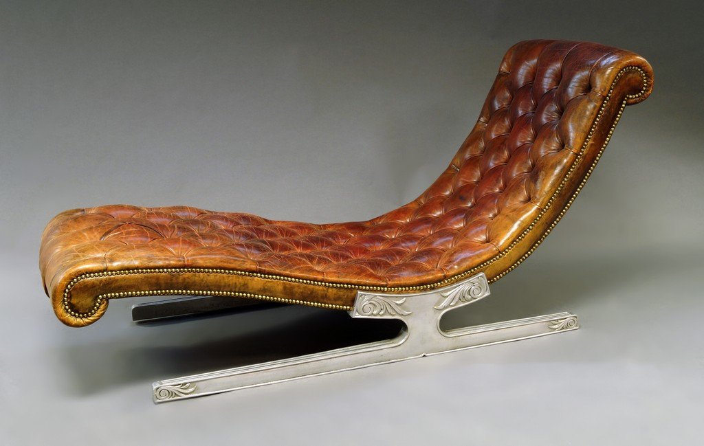 A leather upholstered chaise longue, 20th century, with: A leather upholstered chaise longue, 20th century, with button backed seat, on metal legs