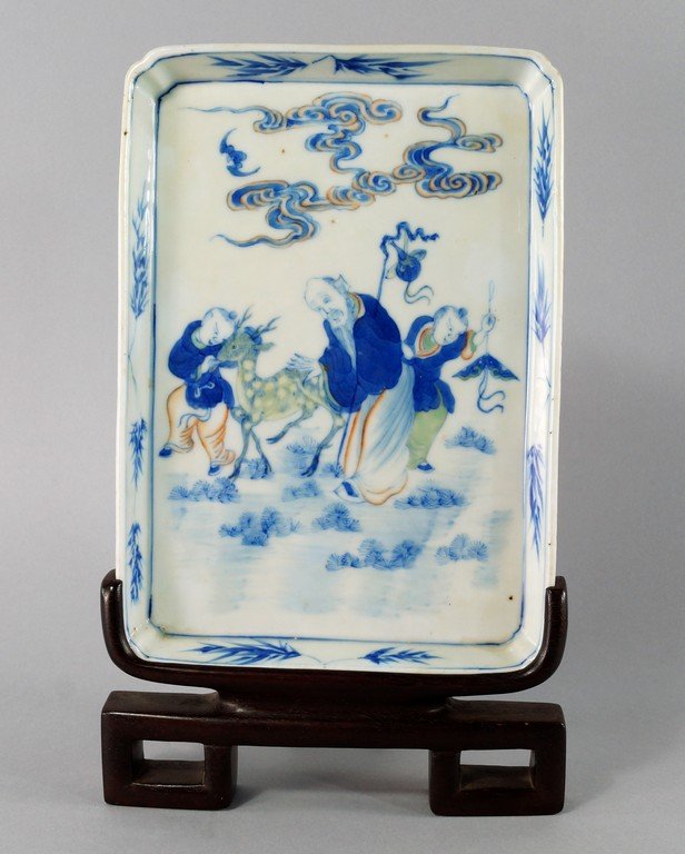 A Chinese porcelain rectangular shallow dish, 19th: A Chinese porcelain rectangular shallow dish, 19th century, painted in underglaze blue with Shou Lao beside two boys and a roe deer, beneath clouds and a bat, inside a bamboo decorated border, 24.5 x