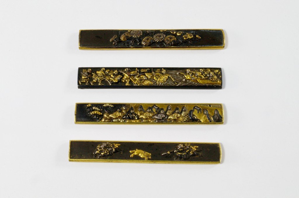 Four shakudo knife handles, kozuka, Goto School, Edo: Four shakudo knife handles, kozuka, Goto School, Edo Period, moulded with friezes of chrysanthemums, battle scenes, a boar hunt and scenes of nobles, 10cm long(4) (VAT charged on hammer price)