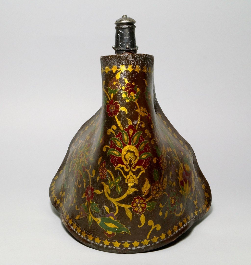 A Turkish lacquered leather flask, late 19th/early 20th: A Turkish lacquered leather flask, late 19th/early 20th century, with grey metal lid and spout, the body with gilded leaves and red and green lacquered flowers and leaves, 27.5cm high