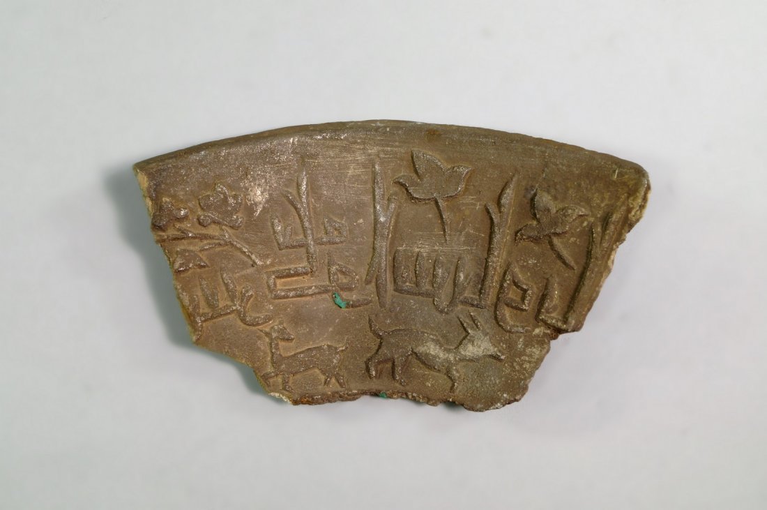 A Middle Eastern fragmentary pottery shard, with raised: A Middle Eastern fragmentary pottery shard, with raised decoration of bands of calligraphy with leaves, above running animals, 12.5cm wide