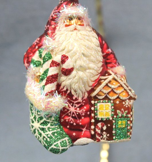 Patricia Breen "Santa for Elaine" Ornament: Patricia Breen "Santa for Elaine-red" Christmas ornament. Santa in red with white spikey trim on cap and on a green stocking on his left. A toy gingerbread house is on his right. His toy sack hangs on