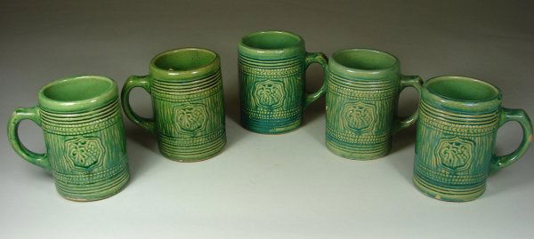 Five Green Salt Glazed Mugs: Grape Cluster in Shield pattern. Three are more teal in color. See page 99 in Salt Glazed Stoneware by Taylor & Lawrance. Two have hairlines at rim, three have rough glaze imperfections on handles one