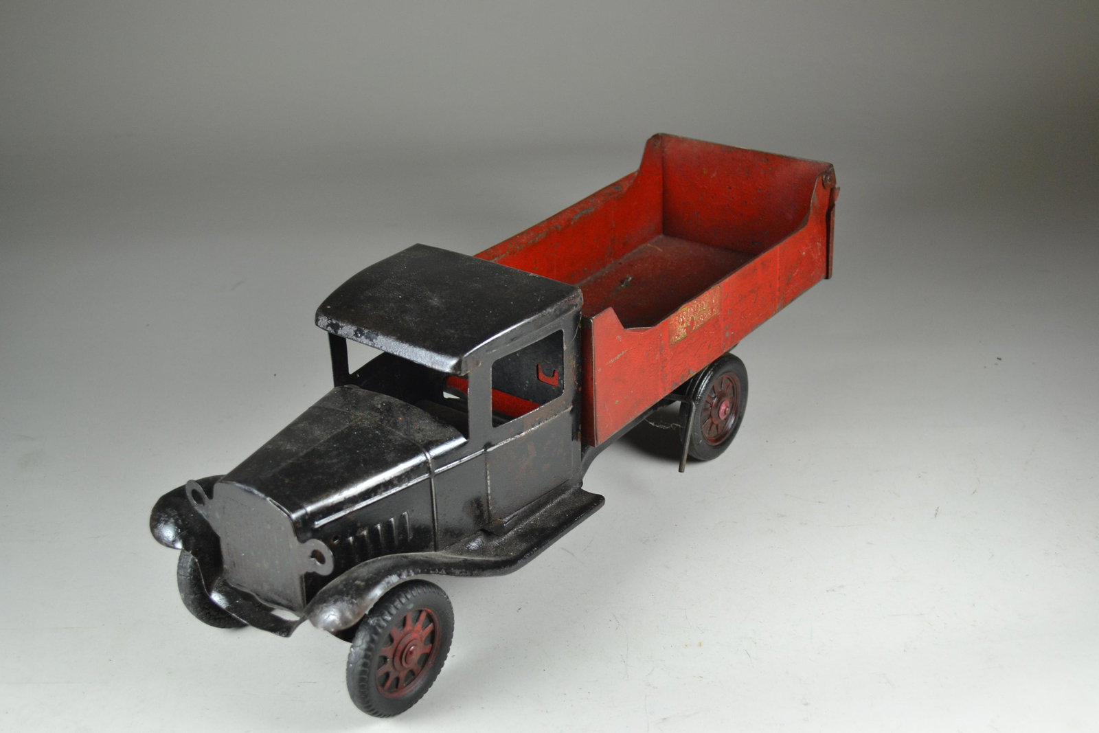 1930's Buddy L Pressed Steel Dump Truck: originally had working head lights. Remnants of original decal. One front tire has heat damage. Moderate wear to paint. 20 1/2" long