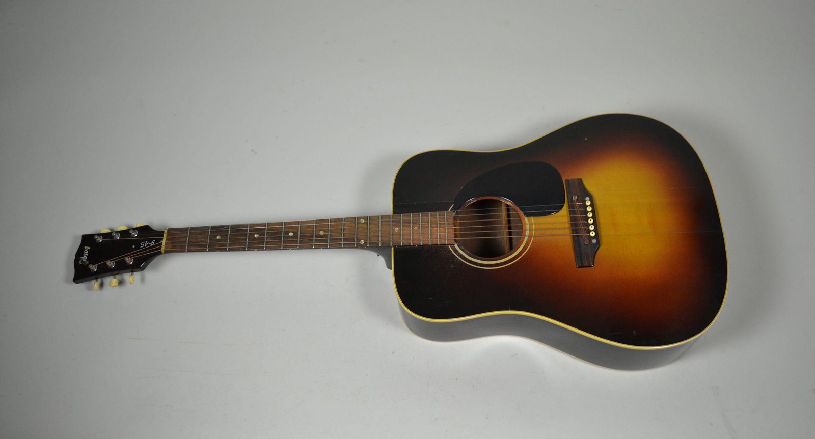 Early 1970s Gibson J45 Deluxe Acoustic Guitar: serial # 972649 and stamped Made in USA. Shows signs of heavy us with wear between frets and has two cracks in front of body. Minor cracking on back side. Missing interior label. Tuners marked Gibson 