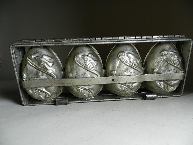 Early Chocolate Mold: in an egg shape with birds and a ribbon on one side. Frame has 4 mold compartments. Wear to mold and dents to eggs. 12" long x 4 1/2" w