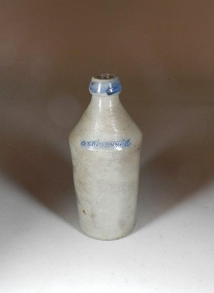 Stoneware Ginger Beer Bottle: marked John Lynch. Has cobalt around top and on name. Minor wear form use. 10' h