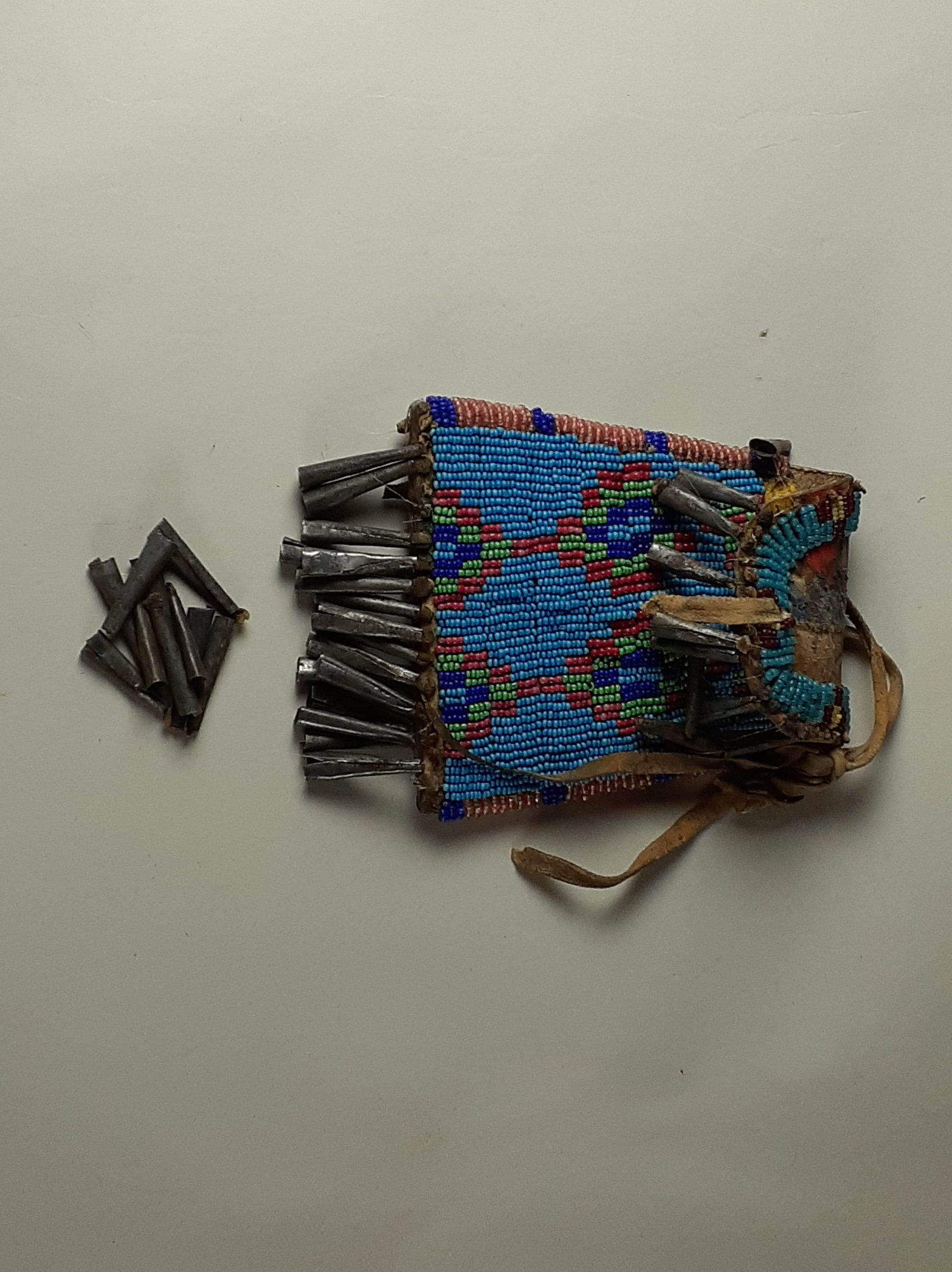 Late 19th Century Sioux Strike a Light Beaded Bag: with metal cone dangles. Buffalo hide bag made from a piece of a larger paint decorated bag. Most of the cones are reattached with fishing line and some are loose. Two holes in back from previous use.