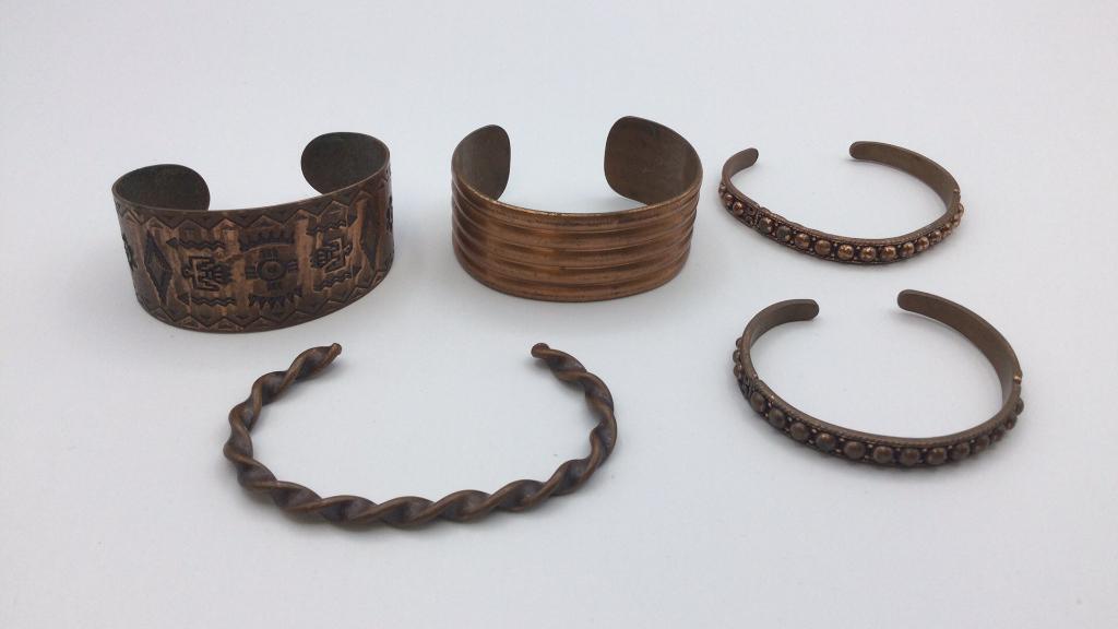 Five Copper Cuff Bracelets: General wear, two are misshapen. Native American stamped design is hallmarked Copper Bell and is 2.25 inches.