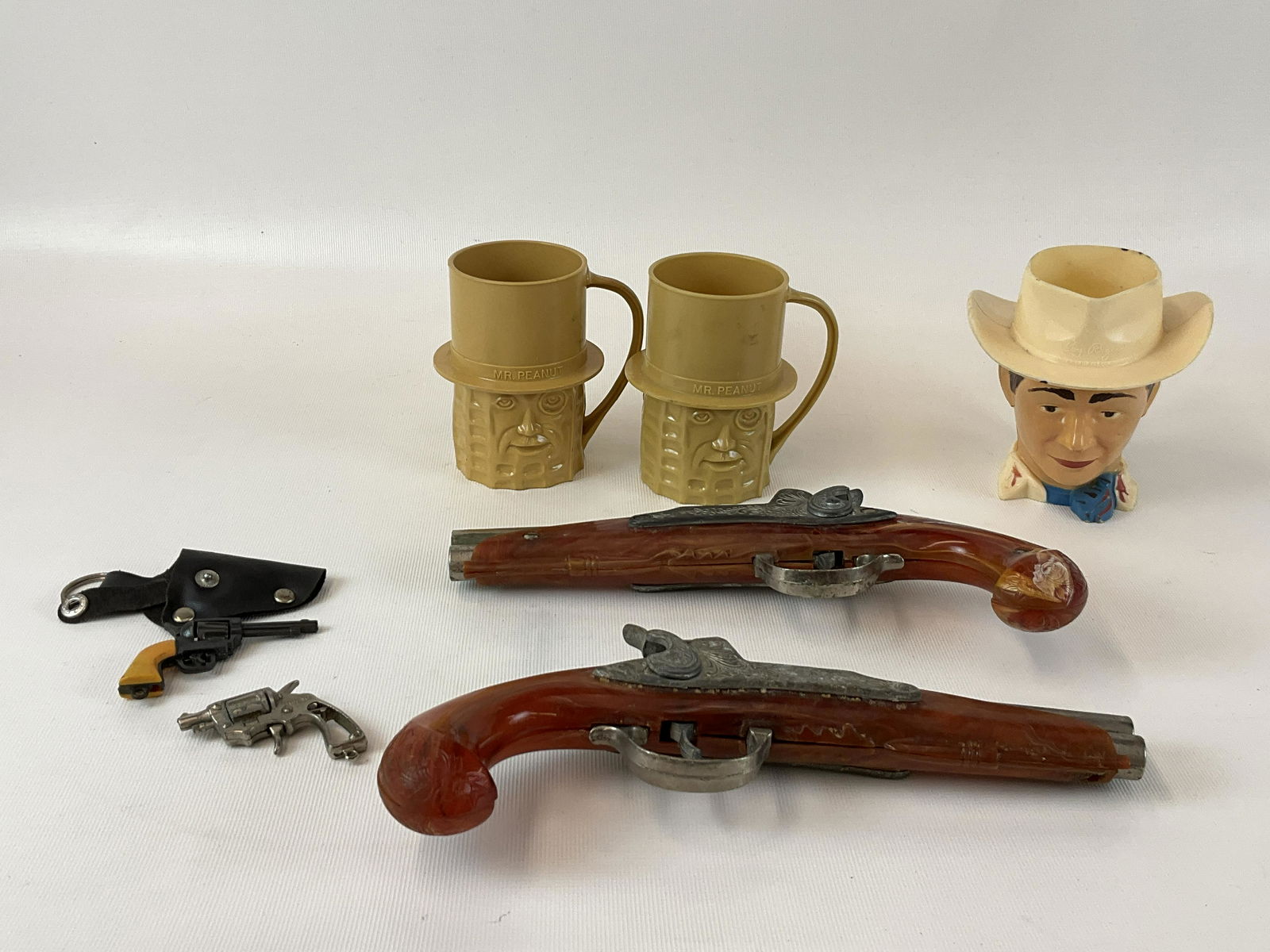 Western Collectibles Hubley Pirate Pistol, Pair Tureno Pistol, etc: Hubley Pirate Pistol Pair Tureno Keychain Pistol Roy Rogers & Mr Peanut Plastic Mugs. Good condition with general wear, one pistol has crack in plastic grip - pistols are 9.5" long