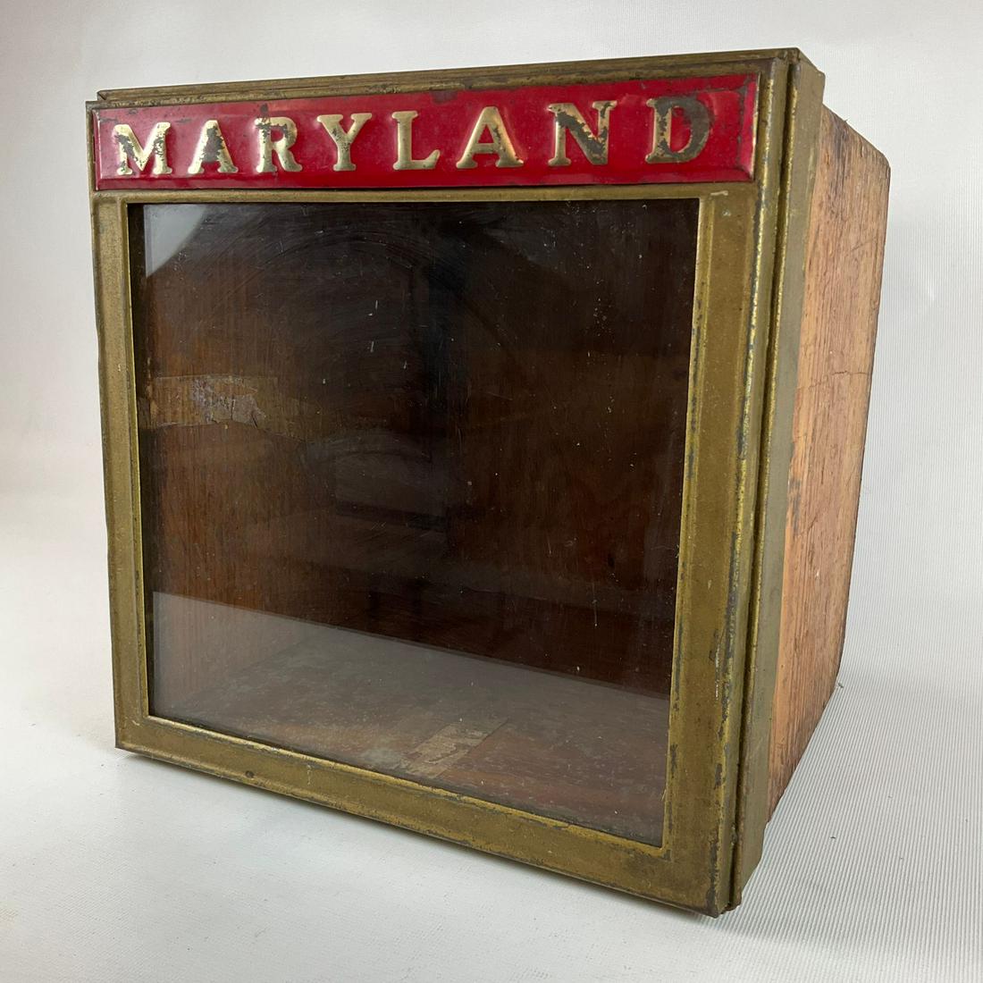 Maryland Biscuit Tin: Wooden box with hinged glass top. Embossed Maryland across the top. Wood has wear and tear, some paint loss on tin. Glass is intact. 10.5 inches wide x 10.5 inches deep x 10 inches tall.