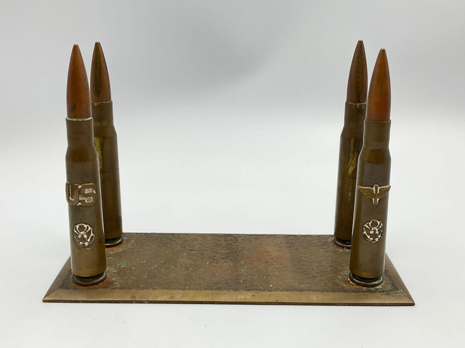 WWII Trench Art Letter Holder: Hammered brass base with four shells. The front two are decorated with Army Air Corps insignia. Good with tarnishing. 8.5 inches wide x 3.75 inches wide x 5.75 inches tall.