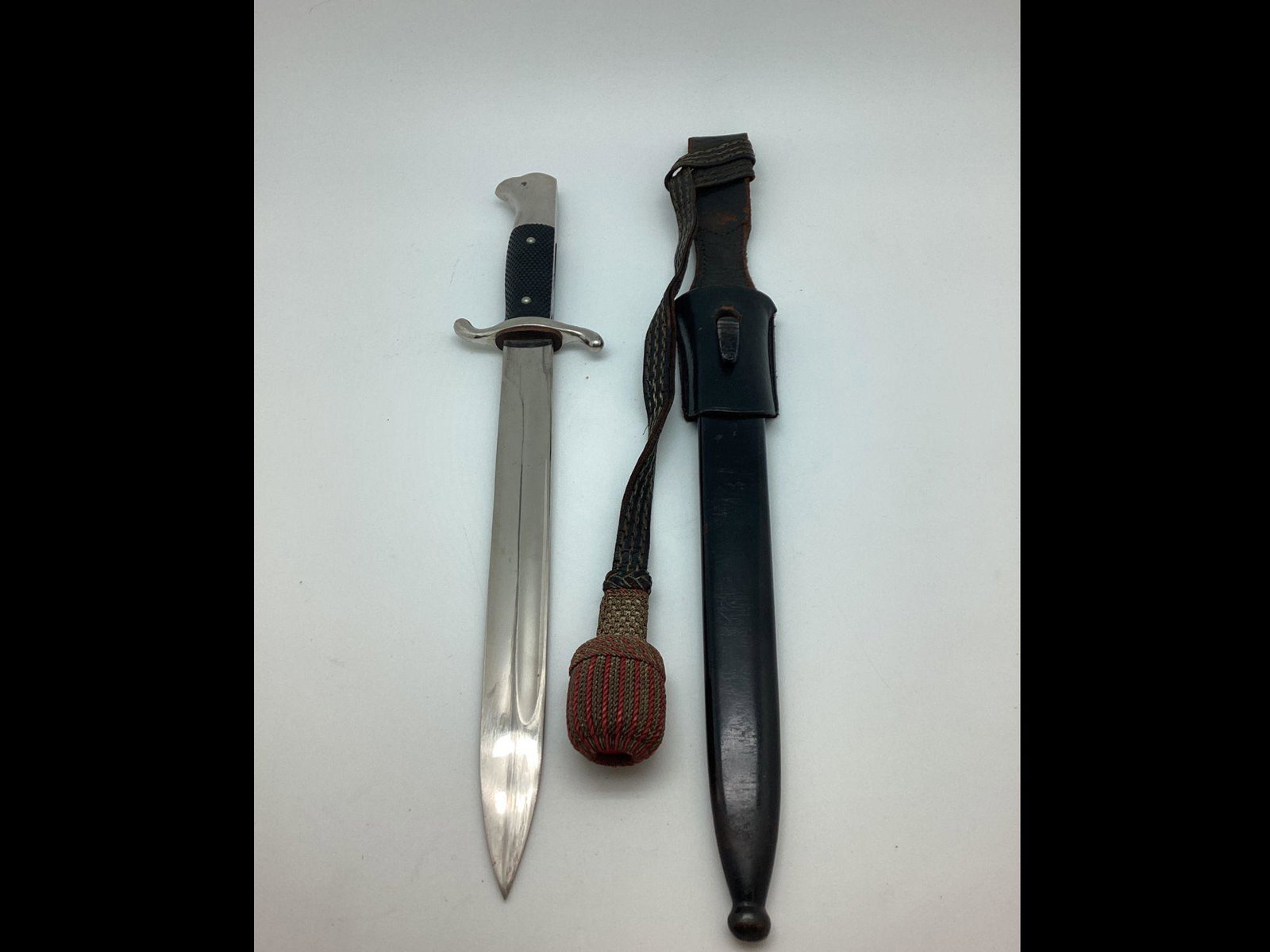 WWII German Fire Police Bayonet Dagger with Rank Knot: Blade is unmarked. Storage wear to blade. Leather frog has areas of wear. Some paint loss to scabbard. Knot is correct with red felt insert. Some wear to bullion wire. Blade 9 3/4" long.