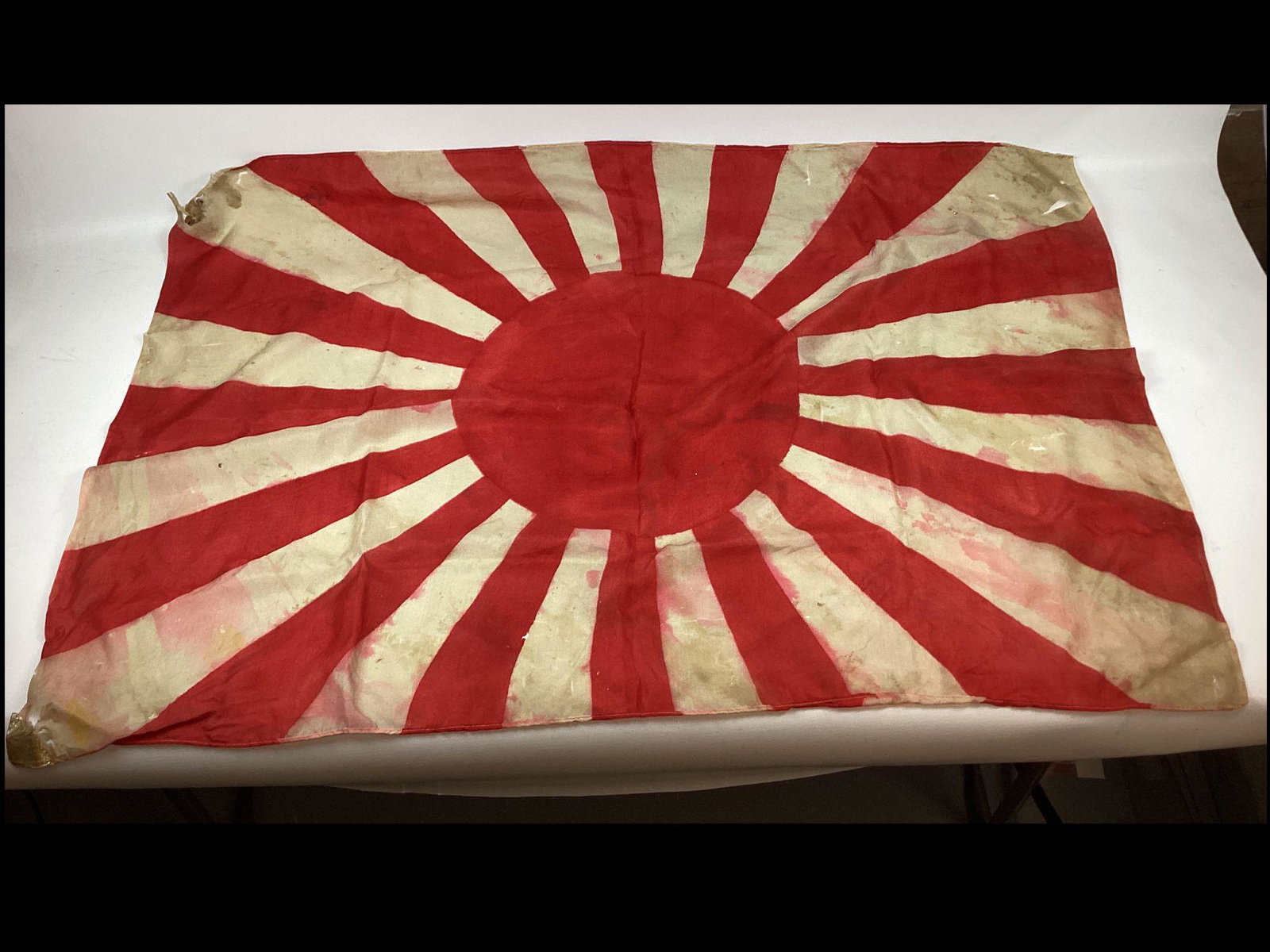 Lot of Two WWII Japanese Silk Flags: The standard flag is heavily damaged with multiple holes and tears. Approximately 37"w x 26" t. The rising sun flag is stained and damaged at the corners. 36"w x 23" t