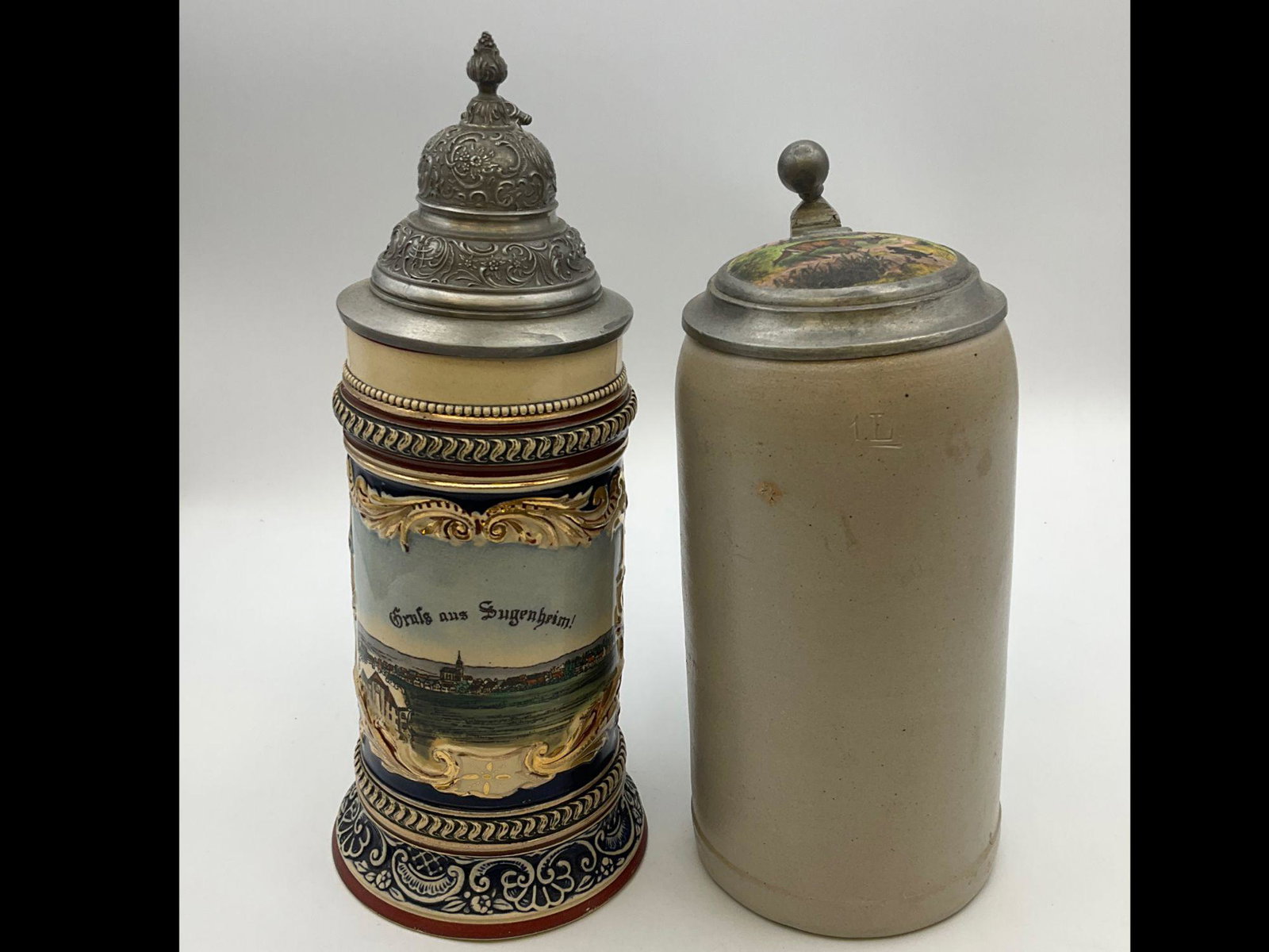 Two German Beer Steins: One marked for G&D with scenic view. Second stoneware1 liter has a transfer stag and dog image on the top. Both in good condition. Tallest is 10.5 inches.