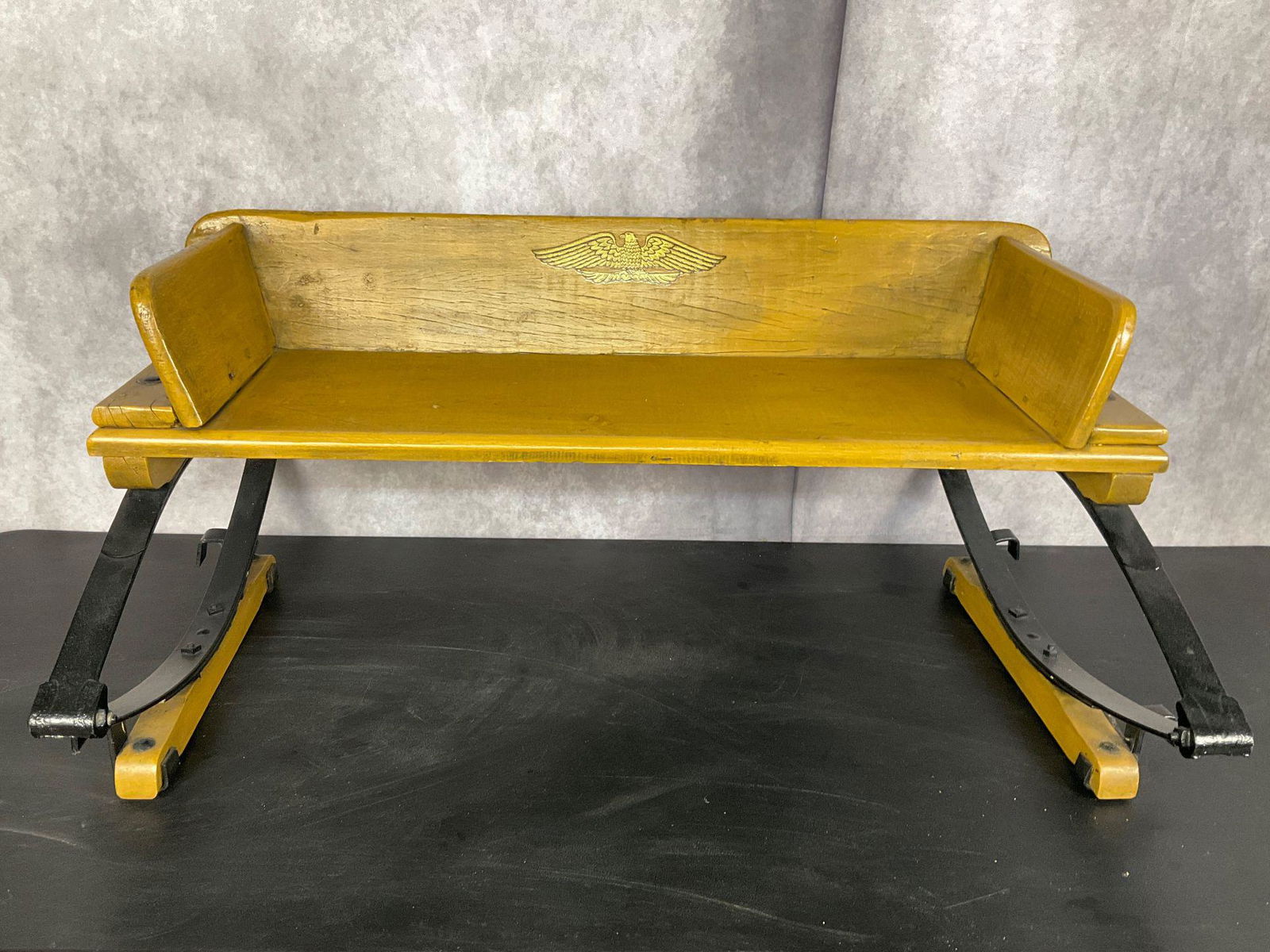 Wooden Wagon Seat: With cast iron hardware. Mustard paint with later added eagle decal. Possibly new bolts. Believed to be an older seat that has been redone. 40.5 inches wide x 26 inches deep x 18.5 inches tall.