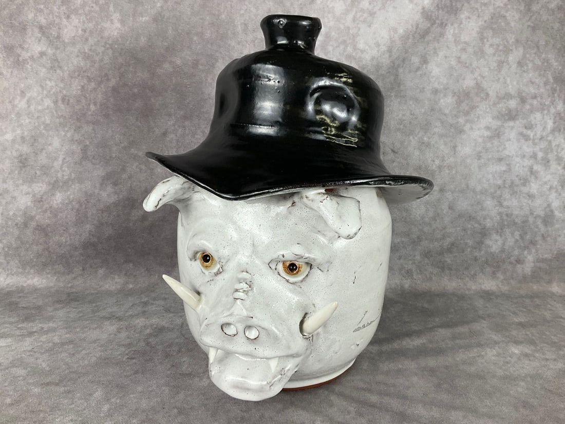 Billy Joe Craven Boar's Head Jug: White glazed boar with tusks, teeth, and a black hat. Jug spout on the hat. Signed. Excellent condition. 8 inches wide x 10.5 inches tall.