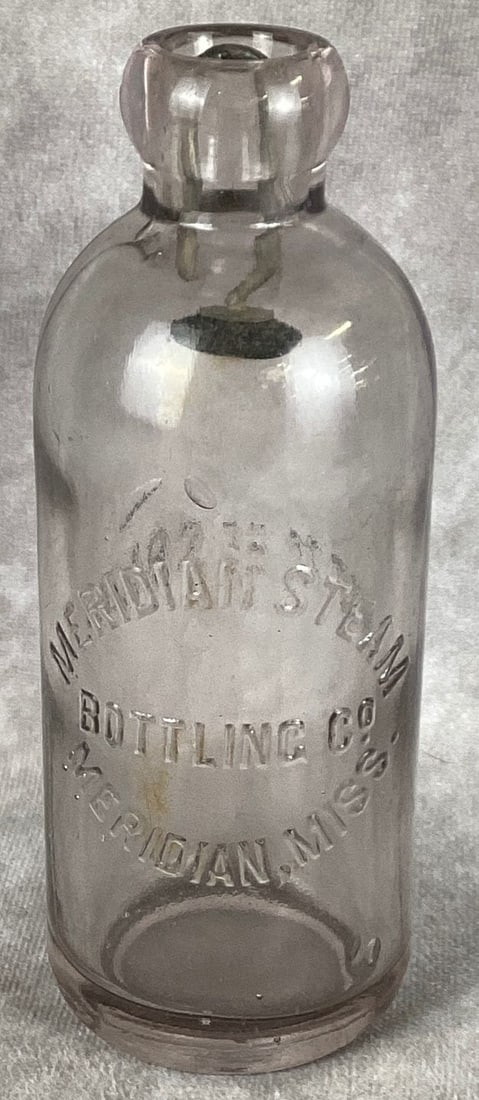 Meridian Steam Bottling Co Meridian Mississippi Hutchinson Bottle: Very lite sun colored amethyst. Small flea bites on lip. Case wear. Has original stopper. 6 1/2” tall