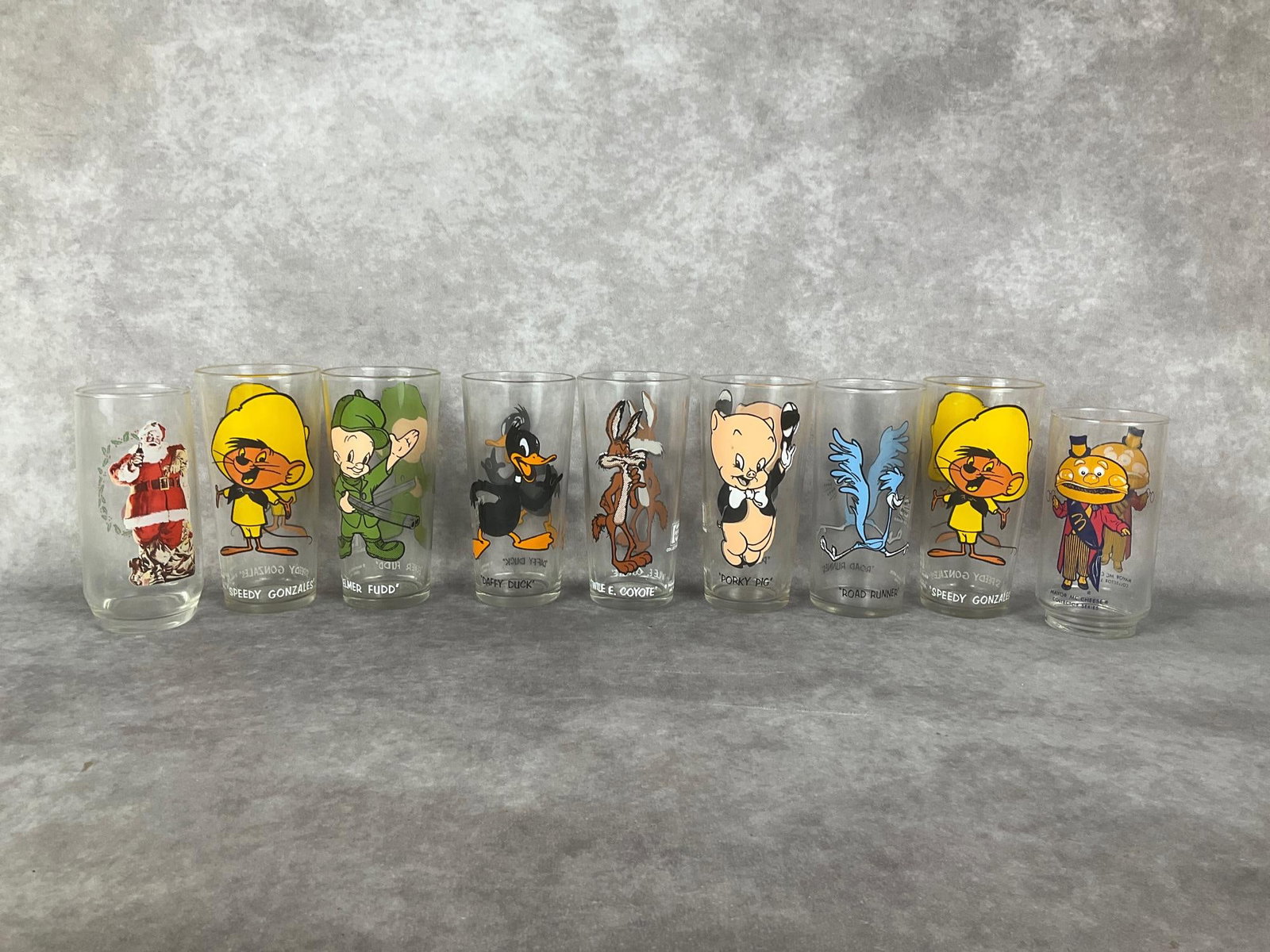 Character Beverage Glasses: Set of seven Warner Bros. 1973 Pepsi Collector Series character glasses featuring Porky Pig, Elmer Fudd, Road Runner, and others. Height of 6.25 inches. Along with a McDonalds Mayor McCheese 5.75 inch