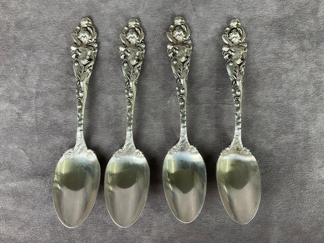 Reed & Barton Love Disarmed Spoons: Group of four. Marked PAT. Appl'd For. Measures 6 inches long. The faces of the figures are worn and have lost their crisp detail. Light scratches and tarnishing. 5.36 ozt silver. No monogram.