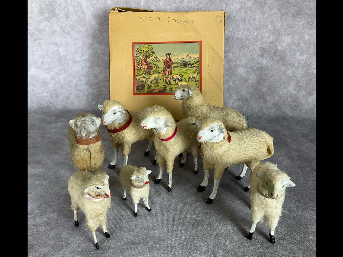 Putz German Wooly Stick Leg Figurines: Group of eight sheep. Some marked Germany. Along with a paperboard box with older Easter grass and lithograph image of sheep, shepherd, and dog. Box is very fragile and torn. Sheep range from fair to