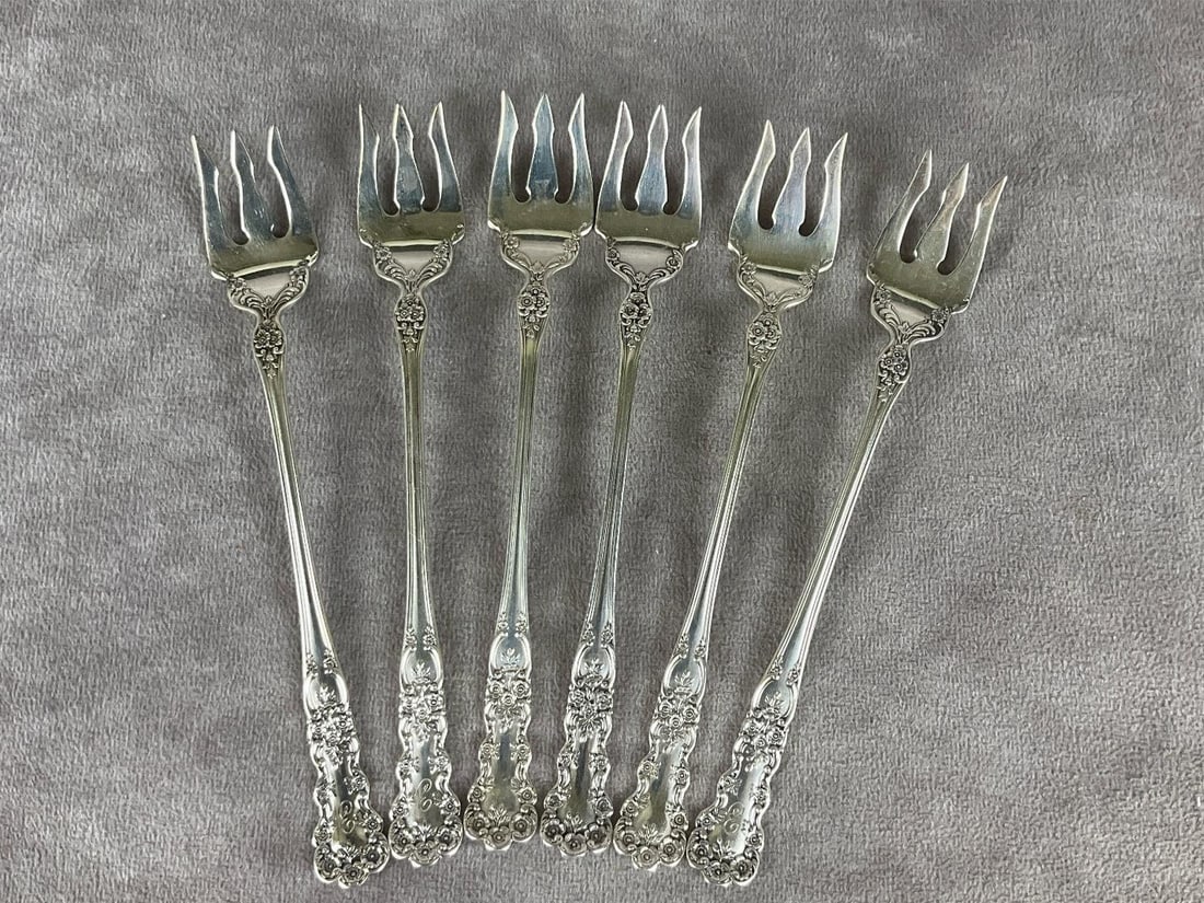 Gorman Buttercup Sterling Oyster Forks: Group of six. Marked sterling. Measures 5 and 1/2 inches long. Light scratches and tarnishing. Three are Monogrammed with E on the front, three are monogrammed with NMP on the back. 2.76 ozt silver.