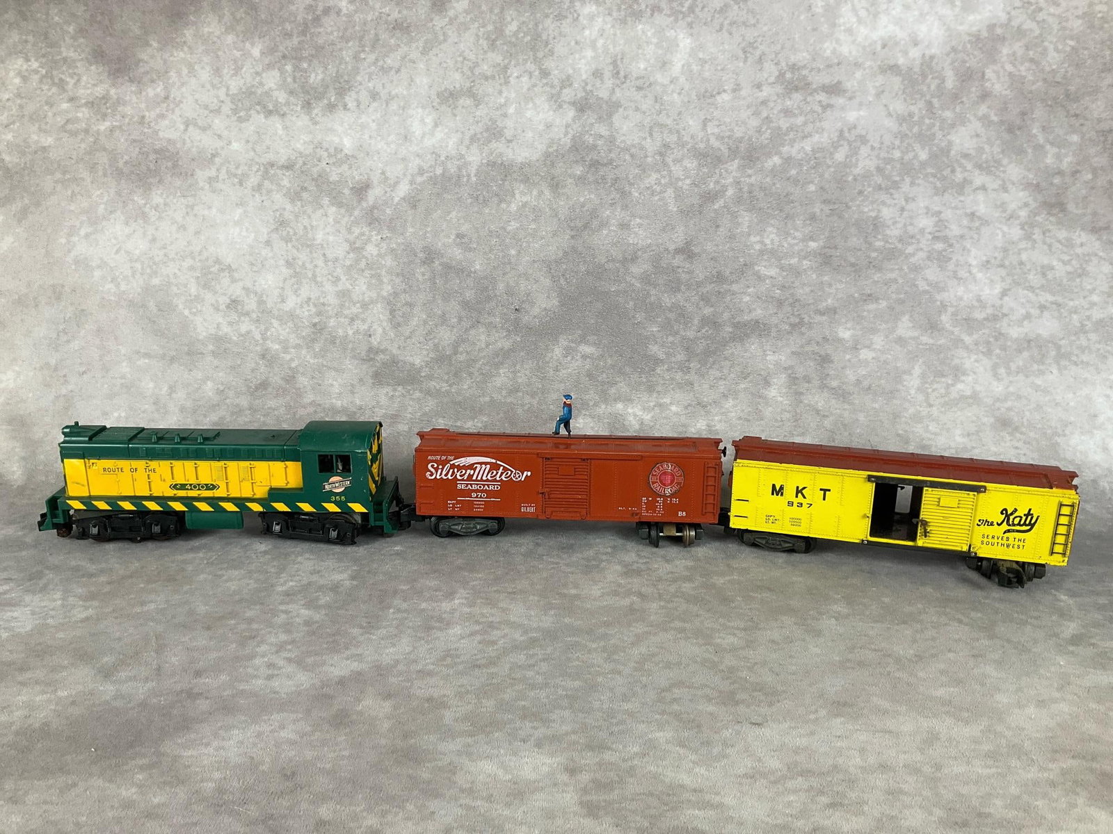 American Flyer Train Cars: Group of three. Northwestern 355, Seaboard 970 and Katy MKT 937. The seaboard 970 has a sliding figure that runs across the top. The Katy has doors that open and close. Fair to good condition with pai