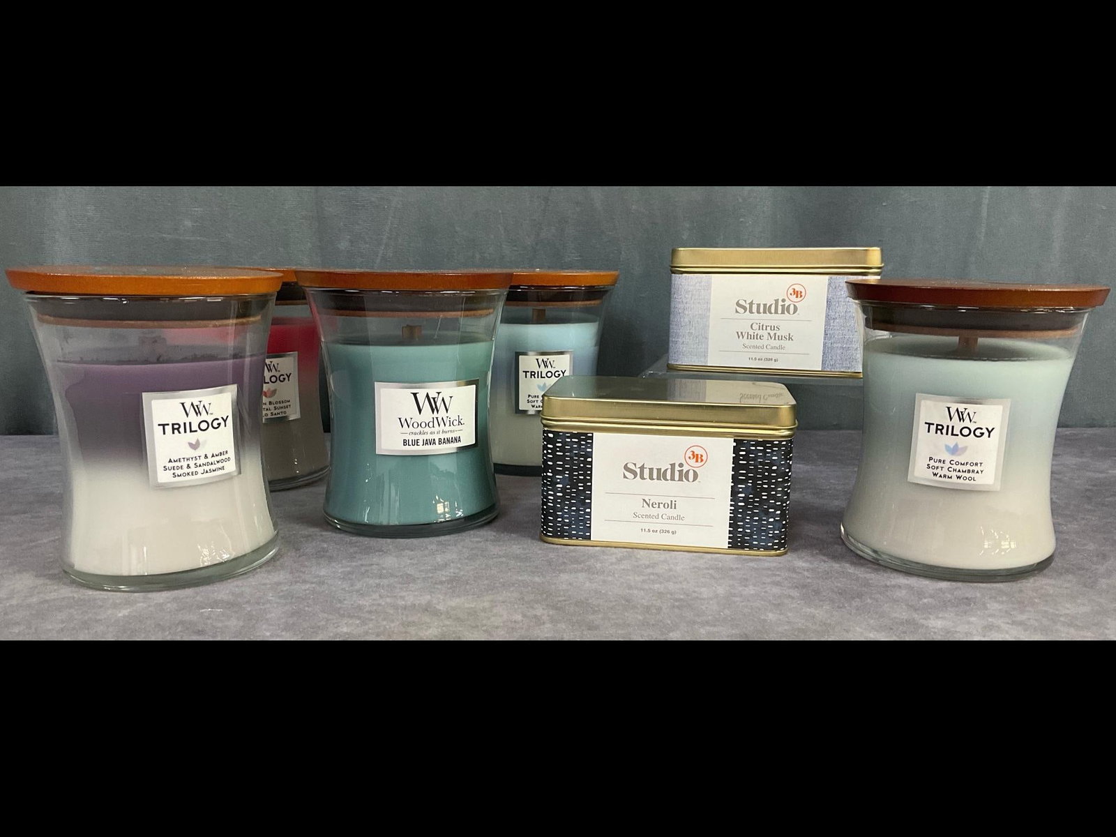 Wood Wick and Bed Bath and Beyond Candles: Group of seven. Four are Wood Wick 9.7 ounce 4.5 inch tall Trilogy candles and one Wood Wick Blue Java Banana. Two Bed Bath and Beyond Studio 11.5 ounce scented Studio 3B candles. Citrus White Musk an