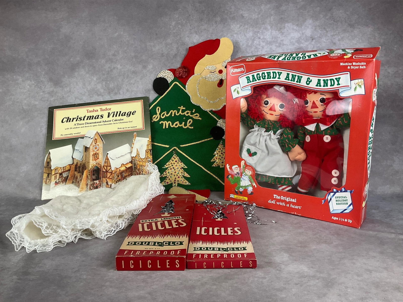 Christmas Decor & More: Two boxes of tinsel, special holiday edition Raggedy Ann and Andy in original box, Tasha Tudor Christmas village 3D advent calendar, Santa mail hanger and cotton tree skirt. Good condition. Mail hange