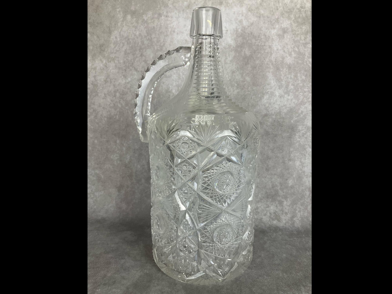 Brilliant Cut Glass Demijohn: Remarkable 15 inches tall. Stepped cut from the neck to the shoulders. Main body with hobstar and palm style. Scalloped cut handle. Inside is fogged on the inside with deposits in the bottom. Some fle