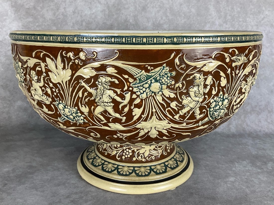 19th C. German Stoneware Punch Bowl: Elaborate design of cornucopias, putto and gnomes with garlands, horns, steins, and grape vines with fruit. No hallmarks but appears to be German made. Mold number on bottom .Crazing throughout. 15 in